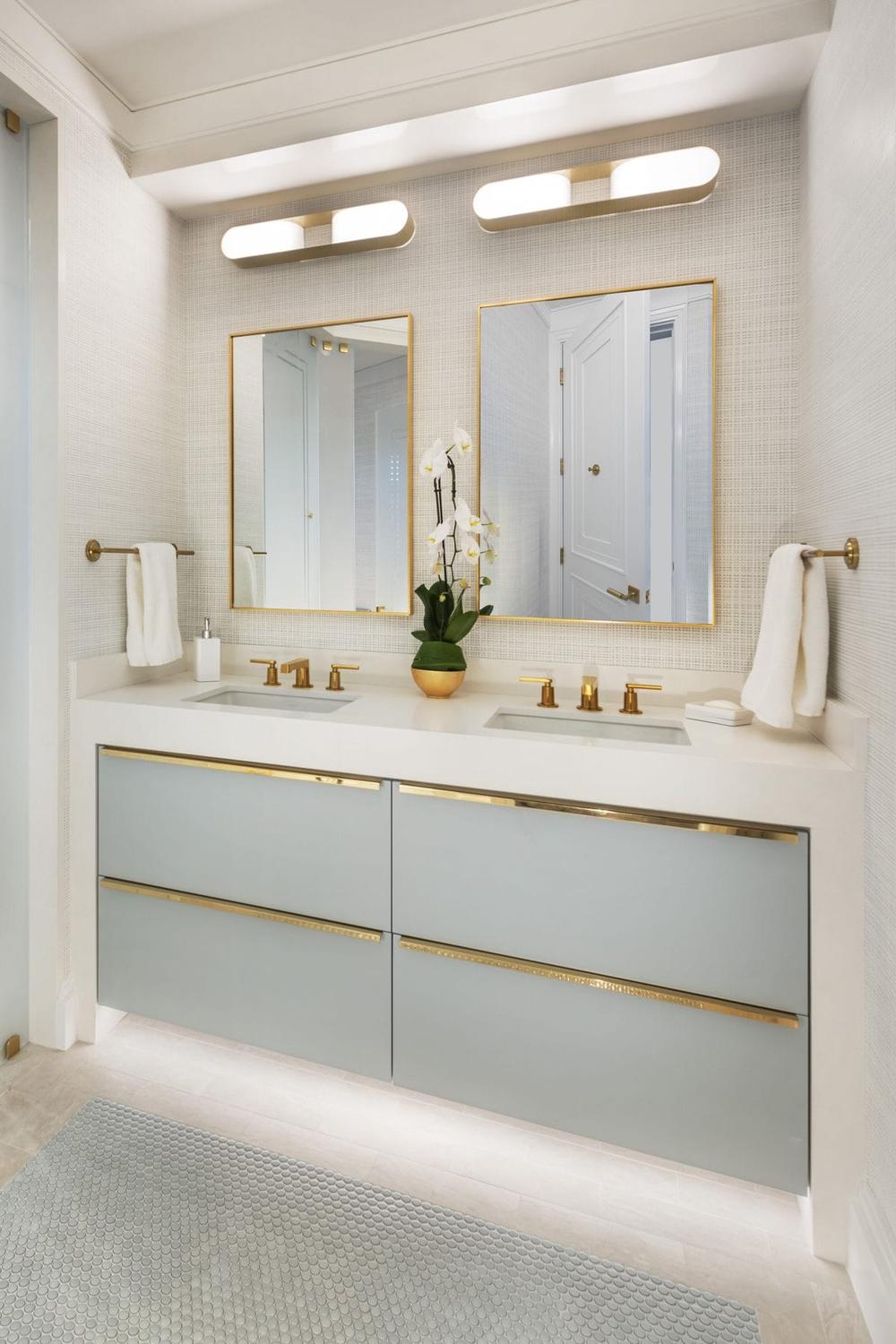 A dual-sink vanity featuring chic gold fixtures paired with textured wall treatment.