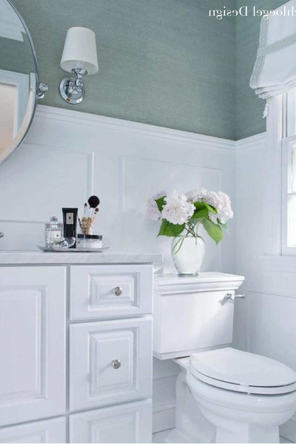 Baño con papel pintado de hierba verde y molduras blancas, mueble de baño y accesorios en tonos elegantes.