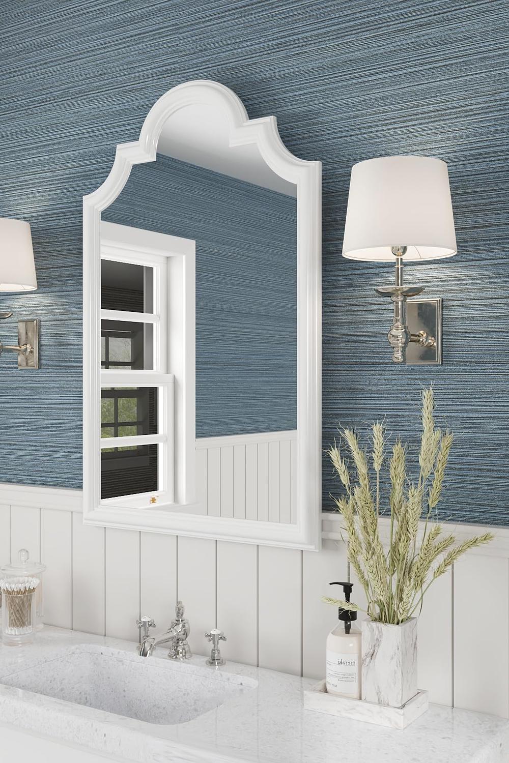 Baño elegante con papel pintado azul, mueble blanco y espejo ornamentado.