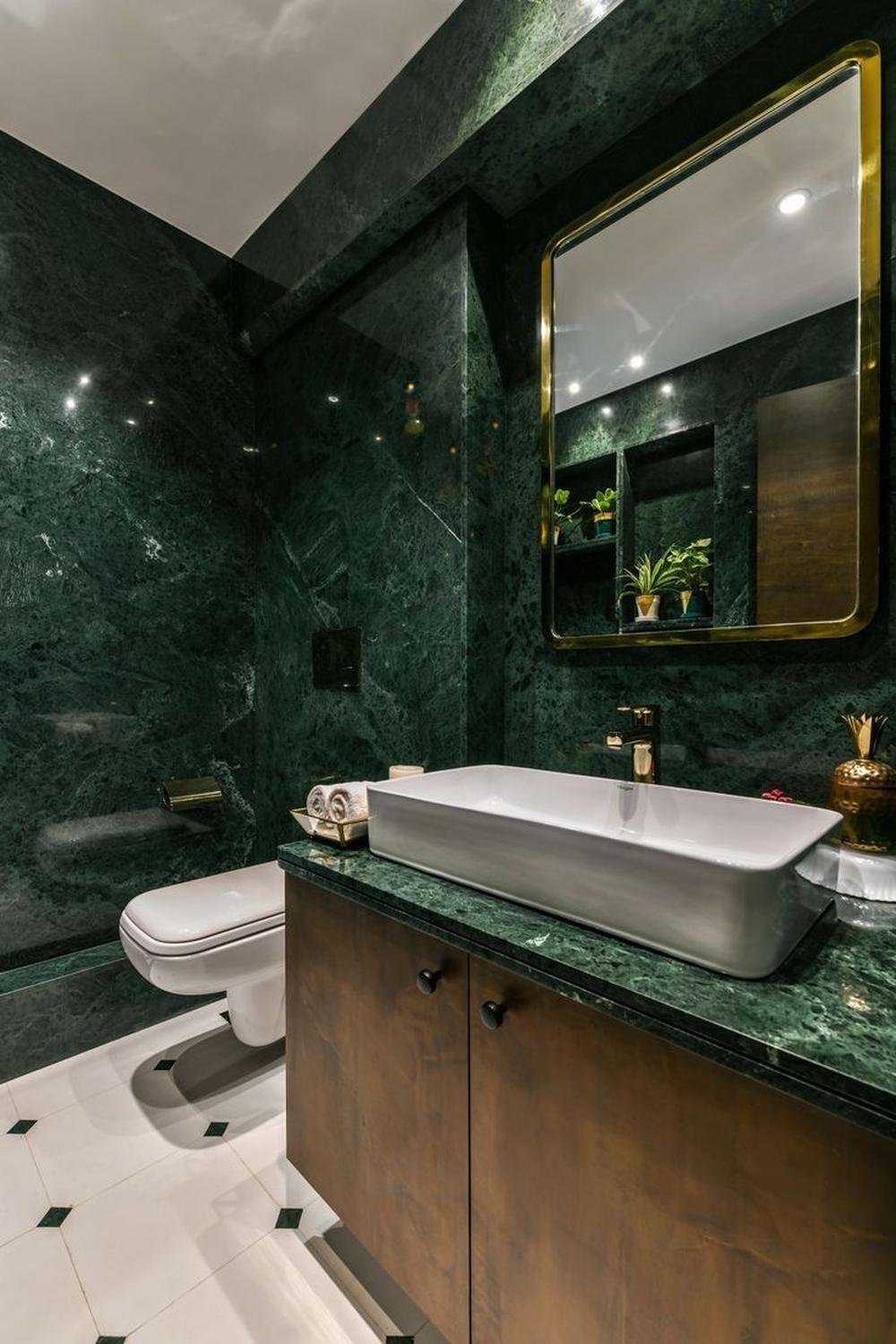 A luxurious bathroom with rich green marble walls, modern oval sink, gold accents, and stylish lighting.