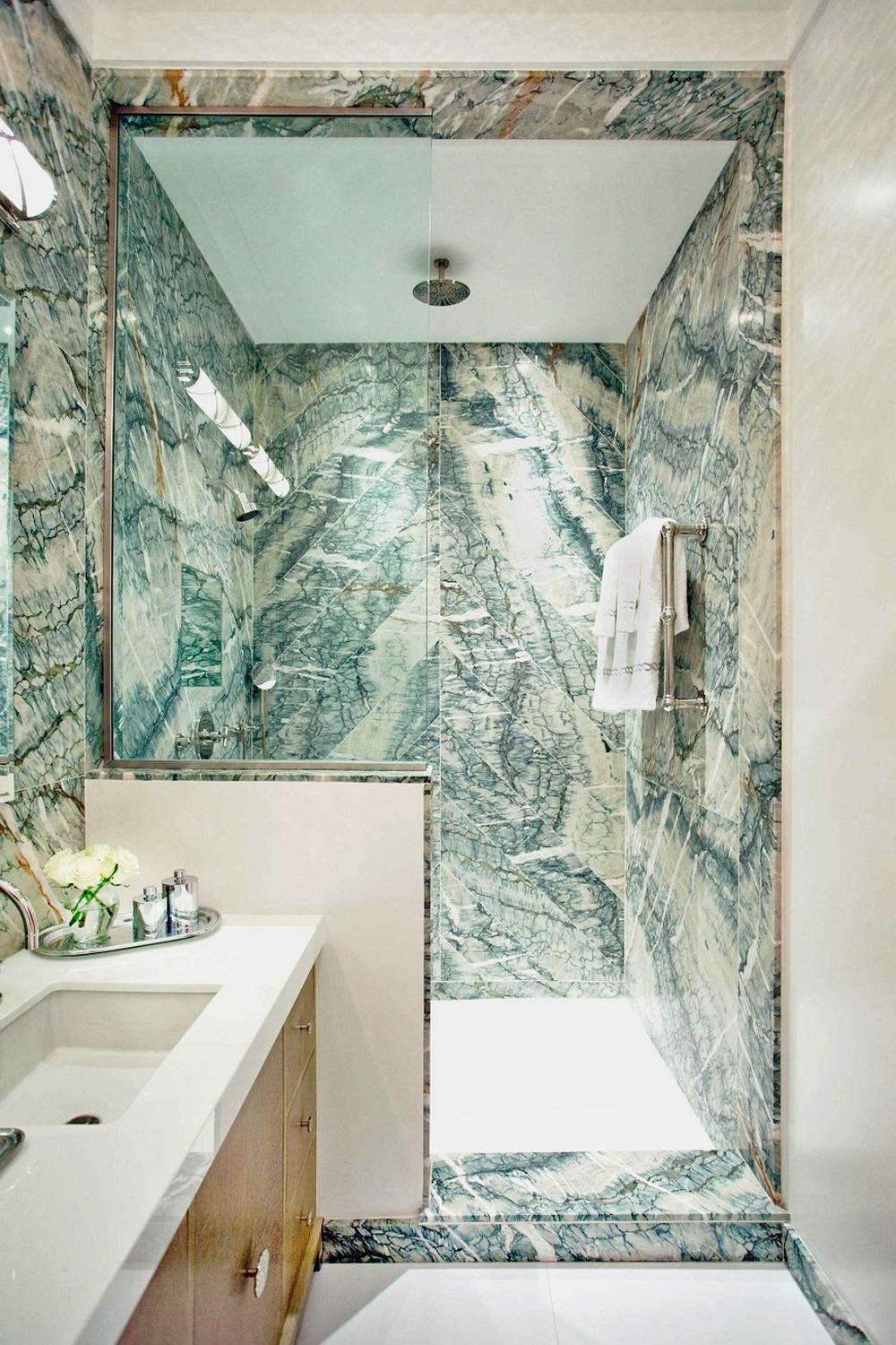 A modern bathroom with green marble shower finishes, elegant white sink, and bright lighting.