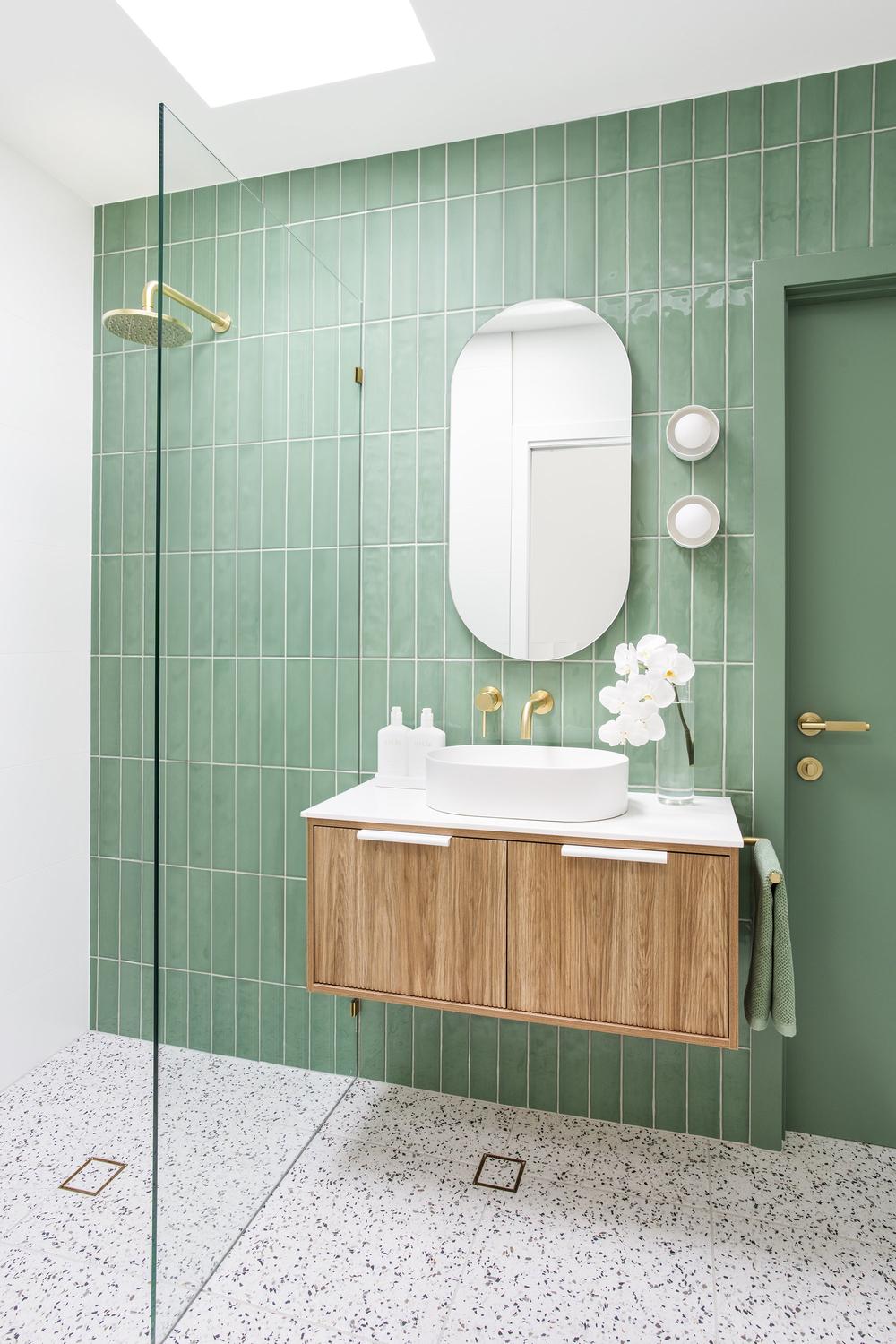 Modern bathroom with elegant vertical green tile walls and sleek wooden vanity.