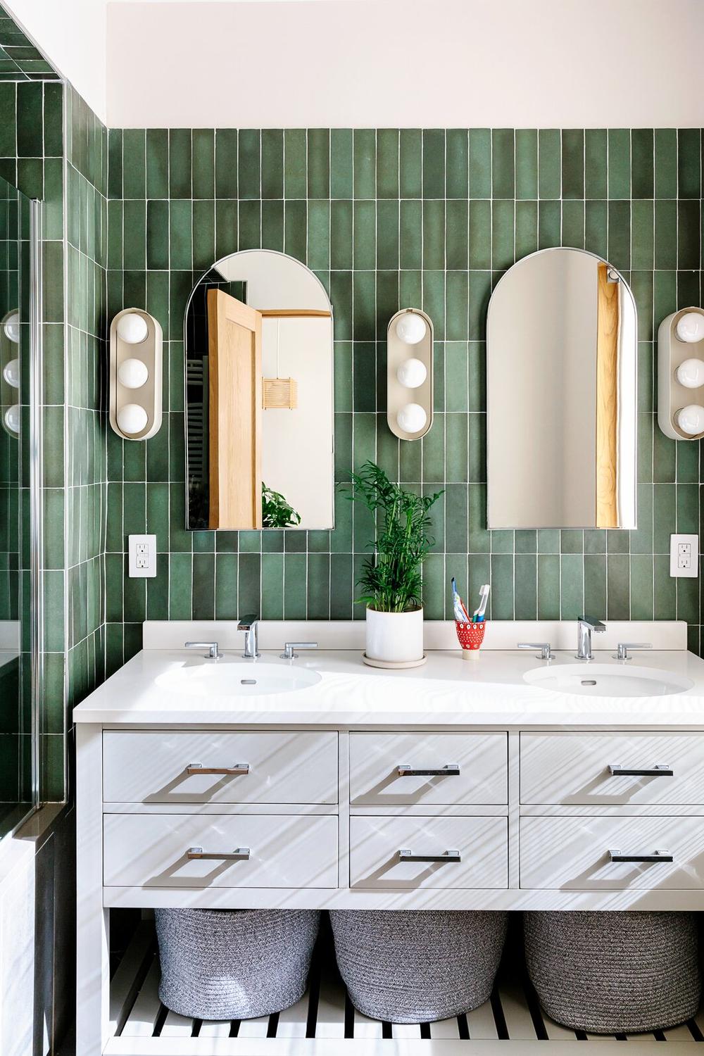 Bathroom featuring large arched mirrors over dual sinks and green tile walls.