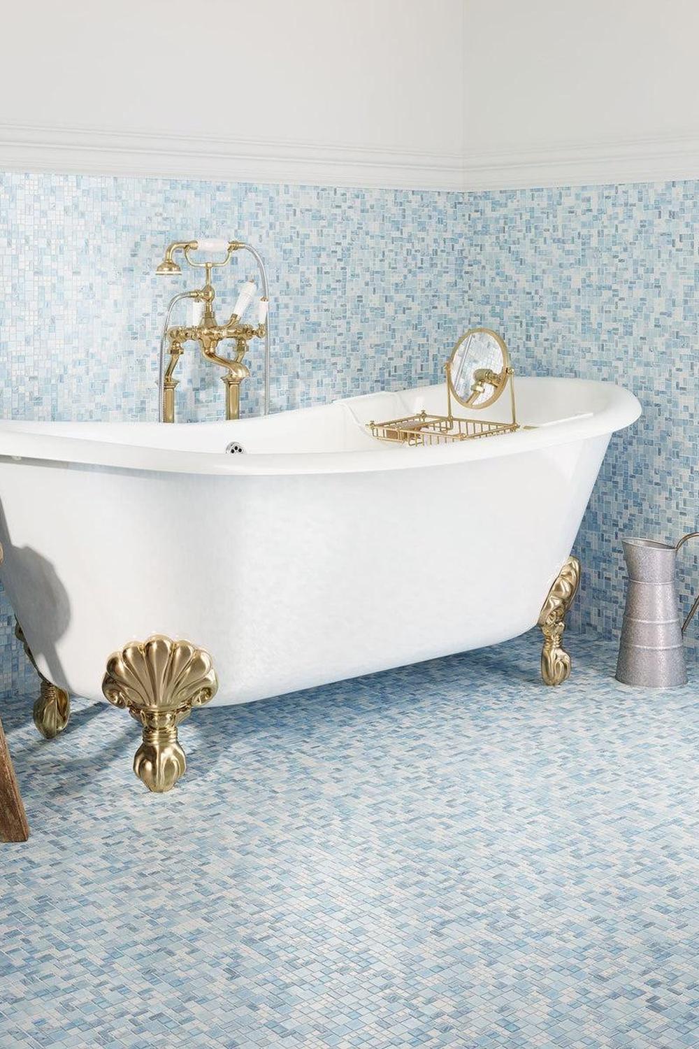 A sophisticated bathroom with a freestanding bathtub, blue mosaic tiles on the half wall, and gold claw feet