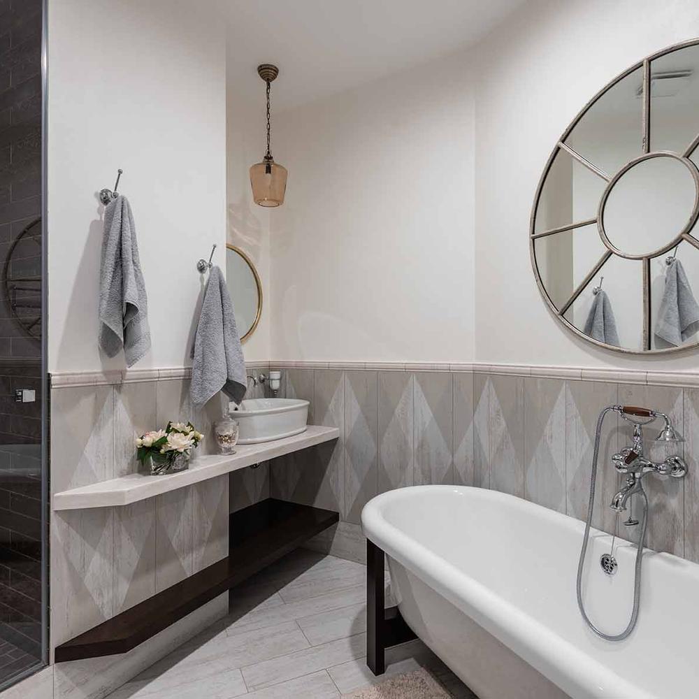 A bathroom with a diamond-patterned gray tile wall, stylish vanity, and a round mirror