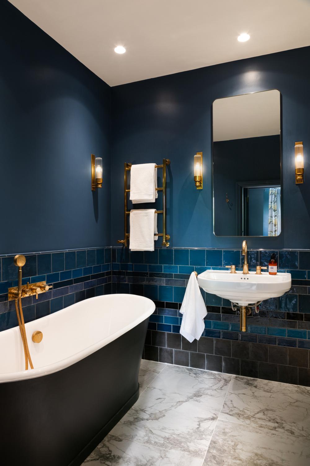 A bathroom with blue and gray tiles, a freestanding bathtub, and gold accents