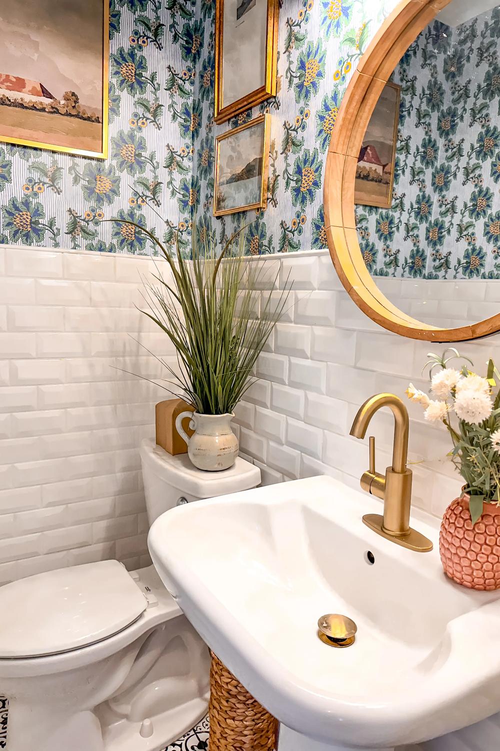 A compact bathroom with floral wallpaper, white tiles, and a modern faucet