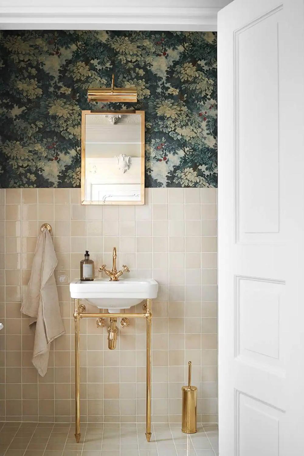 A floral bathroom with beige wall tiles, gold metal accents, and a beautiful mirror