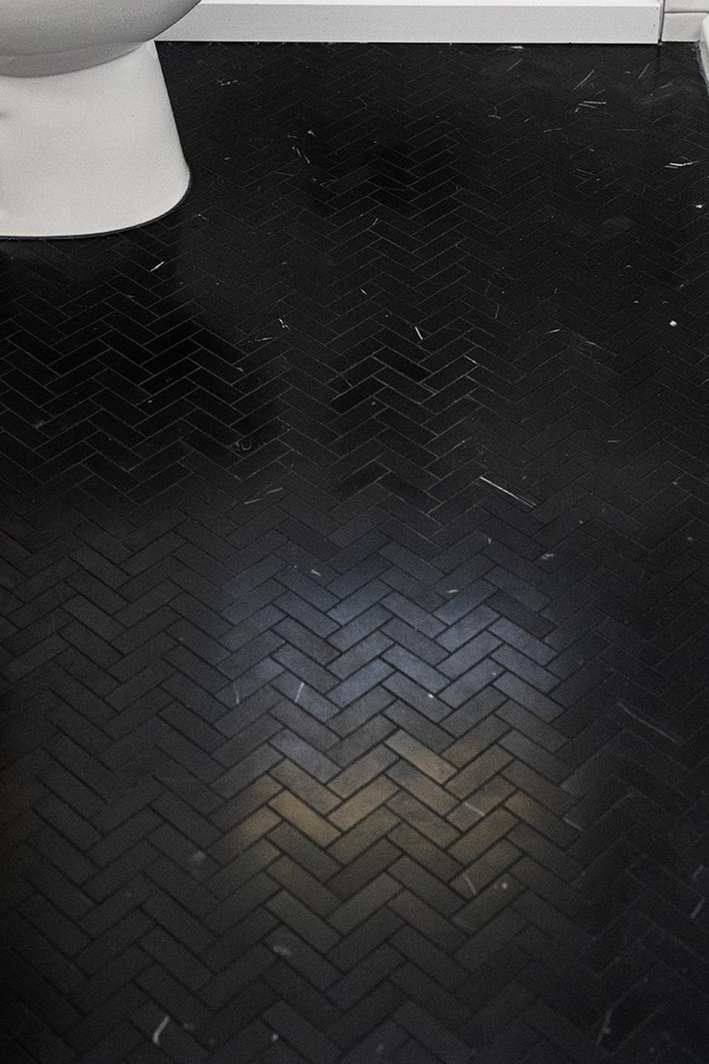 Bathroom floor elegantly tiled with herringbone-patterned black tiles.