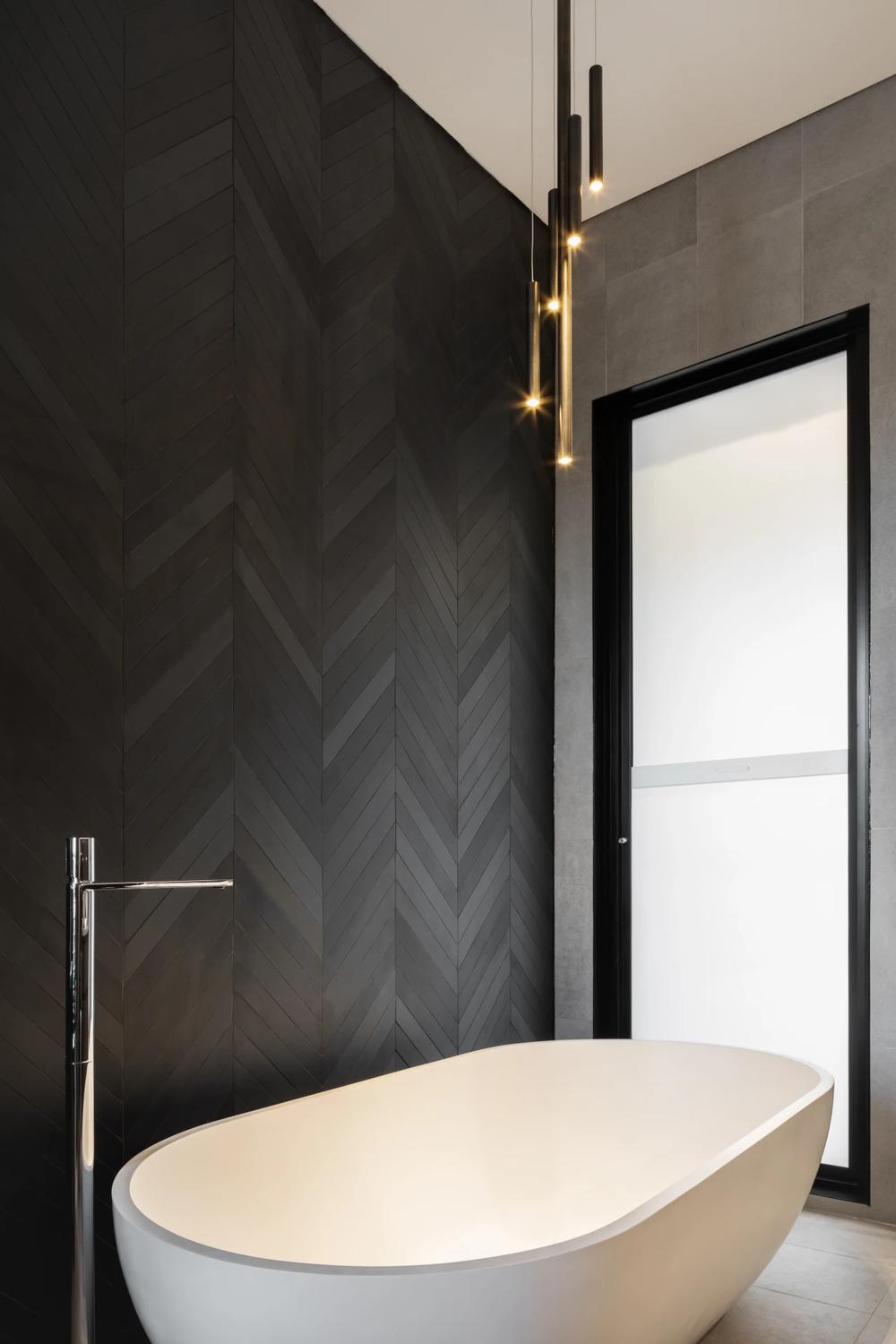 Bathroom design with herringbone black tile wall and freestanding bathtub.