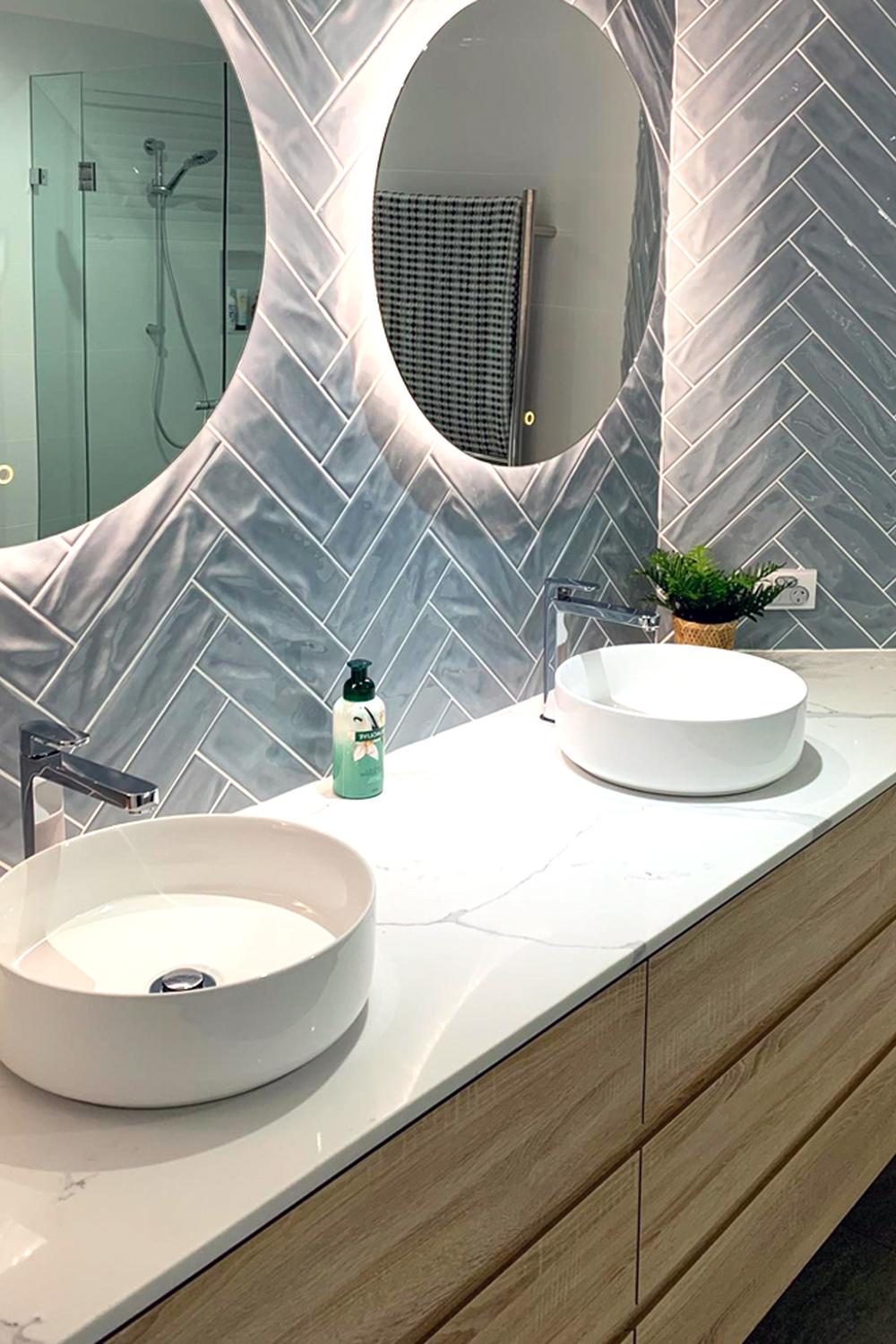 Modern bathroom showcasing light blue herringbone tiles and contemporary sinks with elegant mirrors.