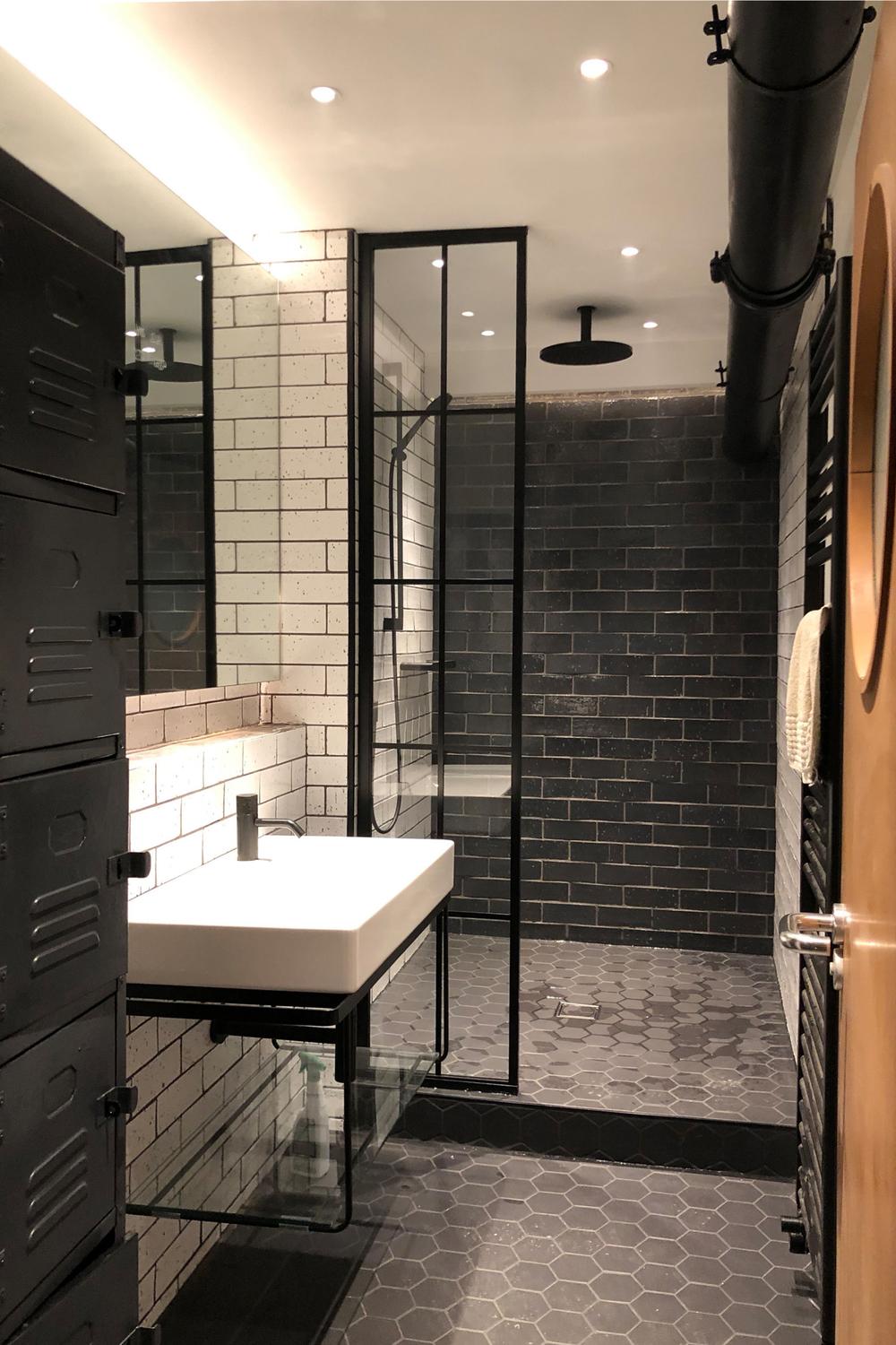 An industrial bathroom featuring dark glossy tiles and a sleek vanity with a round sink.
