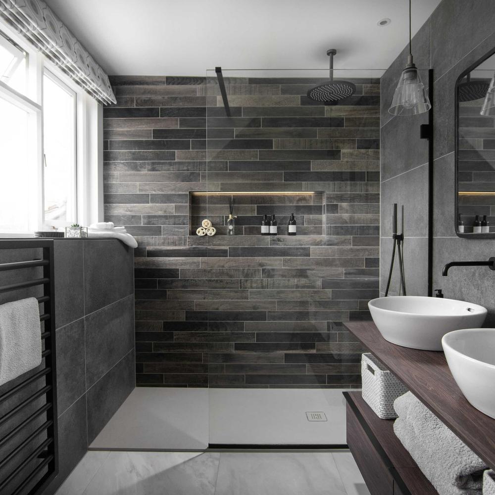 An industrial bathroom showcasing dark textured tiles, a frameless glass shower, and dual basin sinks.