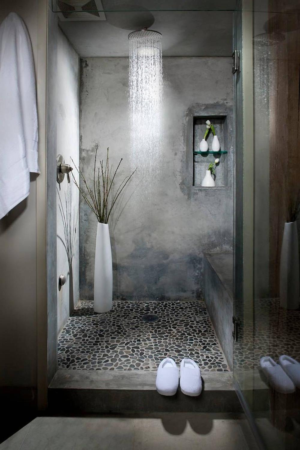 A modern industrial bathroom featuring pebble stone tiles and a soothing overhead shower design.