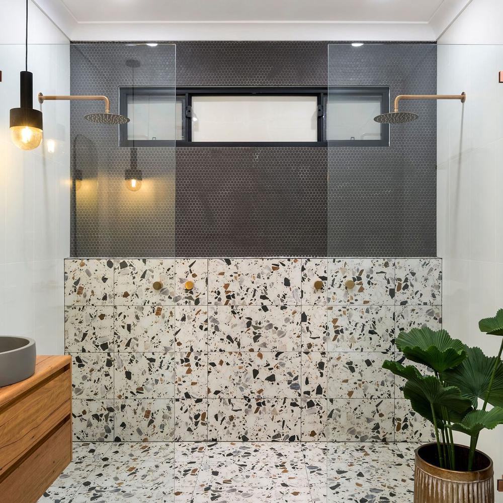 An industrial bathroom with hexagonal tiles, clear glass panels, and a textured wall.