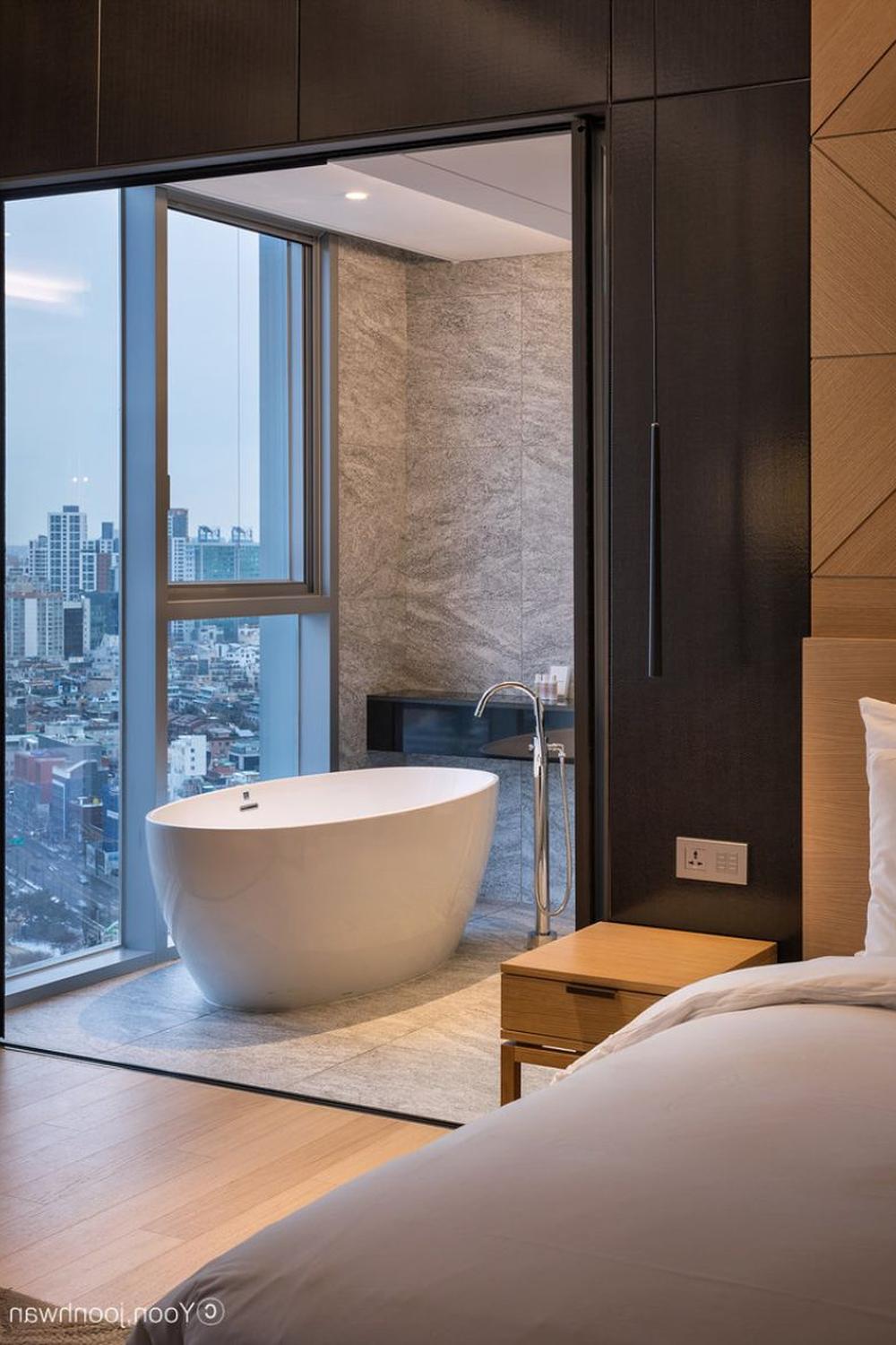 A luxurious hotel bathroom featuring a central freestanding bathtub and a panoramic view of the city, creating an elegant atmosphere.