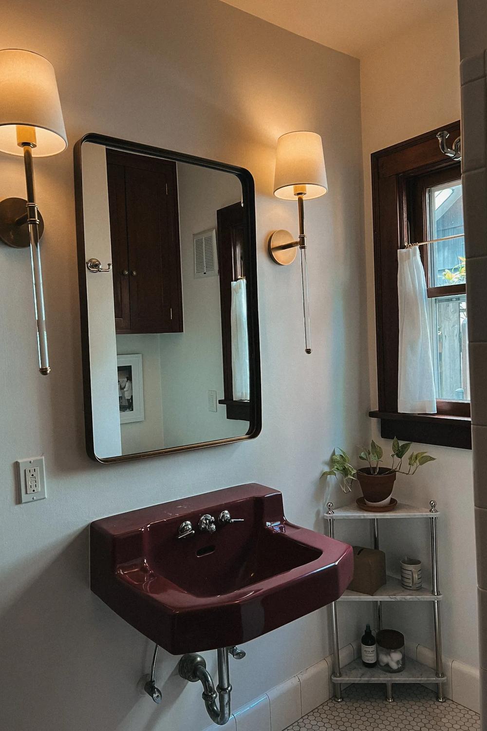 Modern bathroom showcasing the elegance of a deep maroon sink and warm lighting fixtures for a luxurious touch.