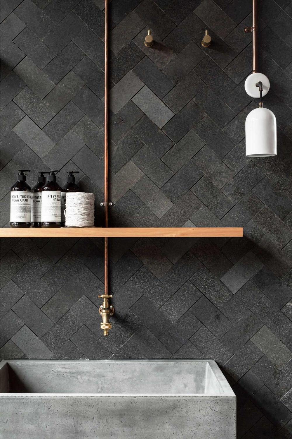 A textured masculine bathroom featuring dark tiles arranged in herringbone patterns.