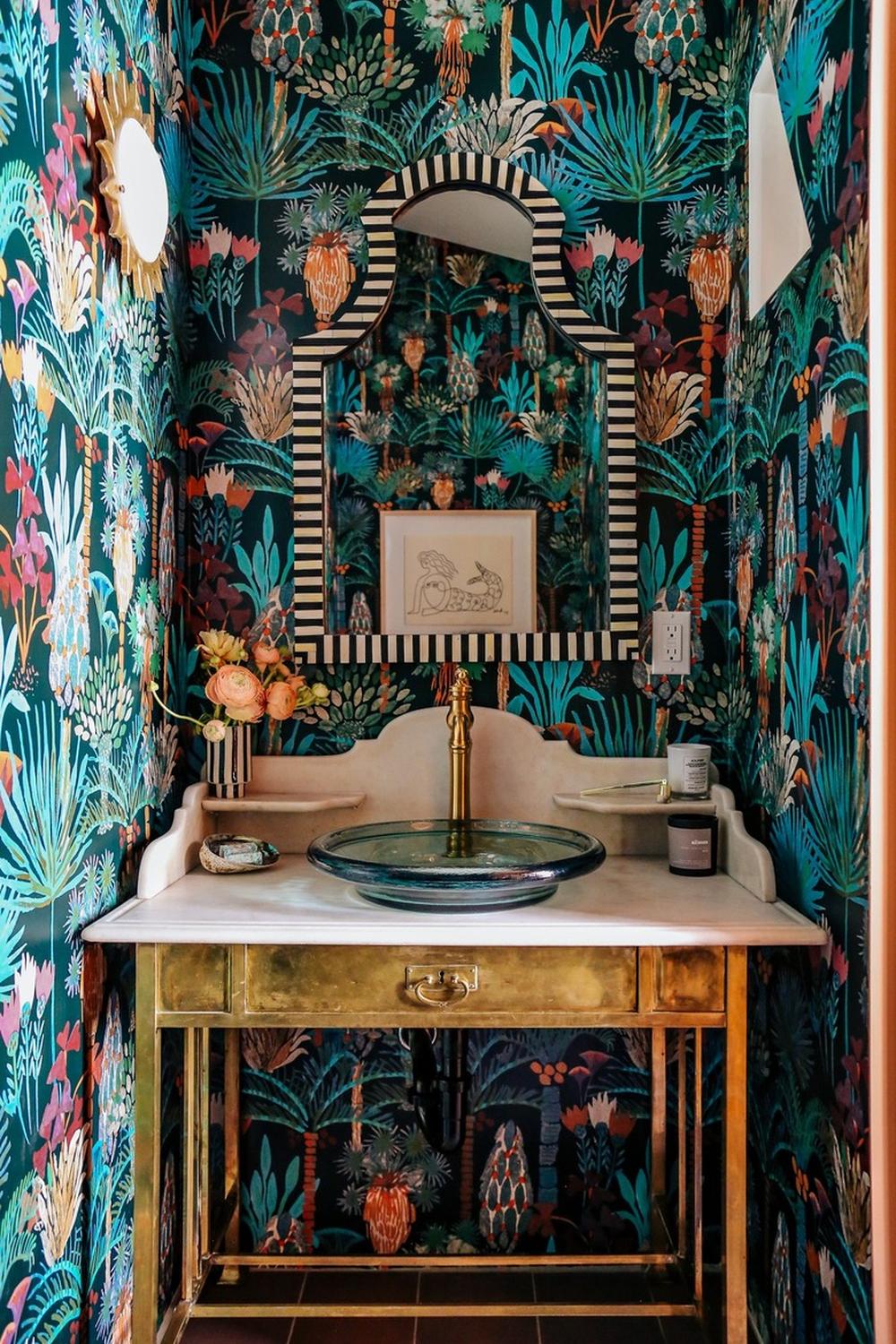 Striking dark teal bathroom with patterned wallpaper and artistic mirror.