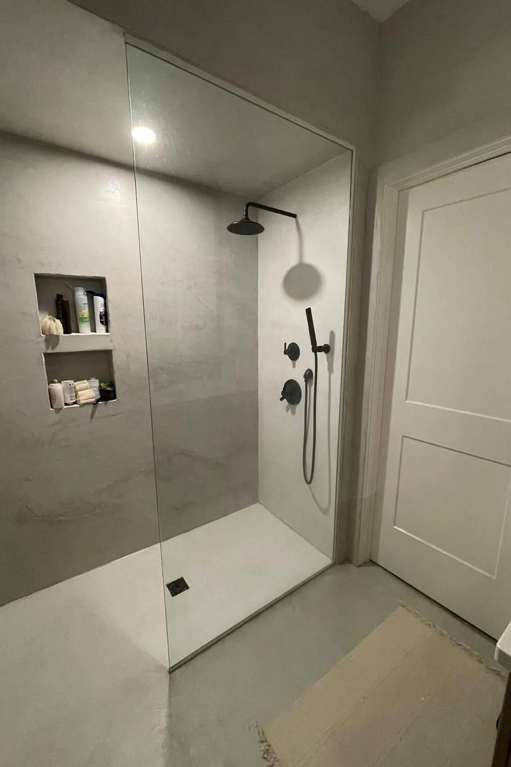 Shower area featuring an open design with micro cement and glass panels.