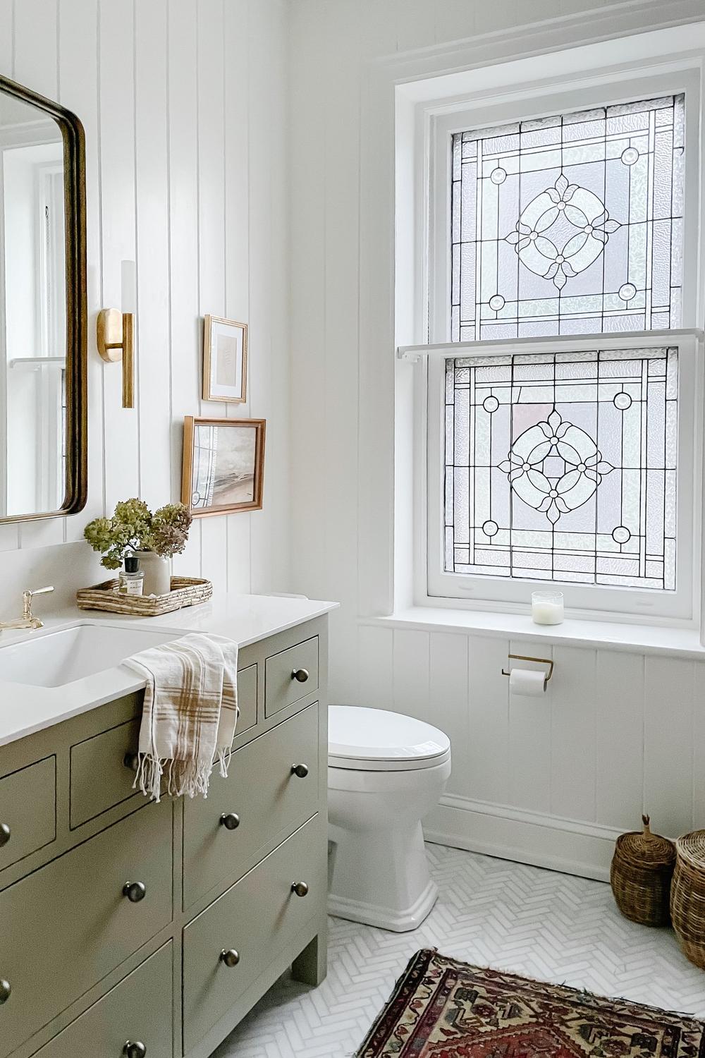 A light and airy modern cottage bathroom featuring olive green cabinetry, smooth countertops, and stylish accents.