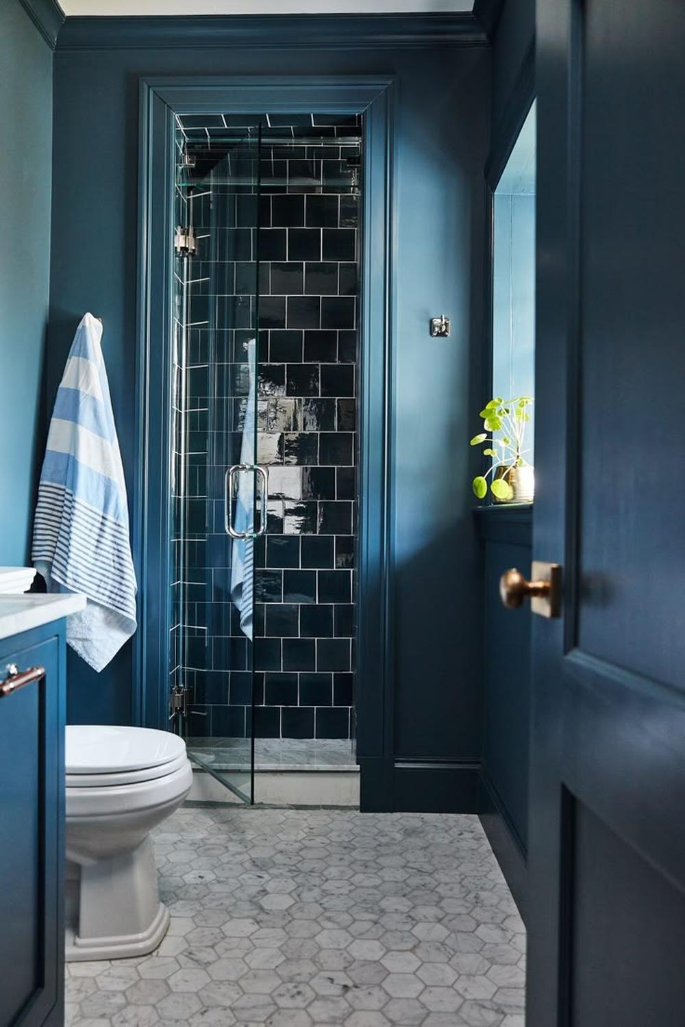 A moody blue bathroom with dark blue walls and light blue accents featuring a modern shower area and elegant vanity.