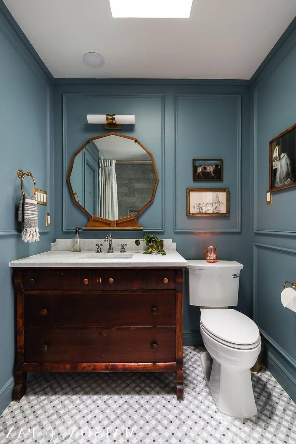 A vintage-inspired moody blue bathroom with recessed paneling, modern light fixture, and classic mirror.