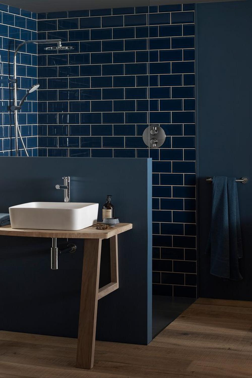 A modern moody blue bathroom with glossy subway tiles and a light wooden vanity.