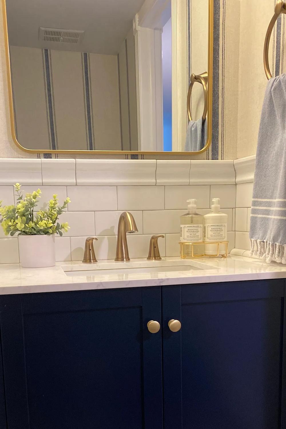 Baño con mobiliario azul marino y detalles en dorado que aportan elegancia