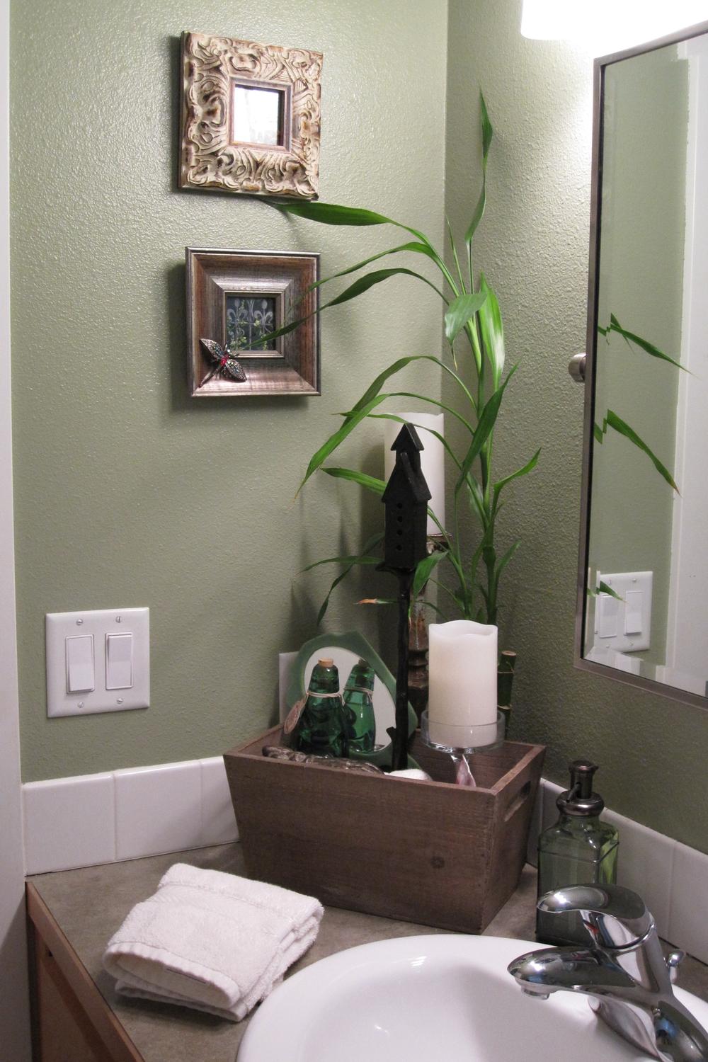 A compact olive green bathroom featuring decorative frames and natural elements.