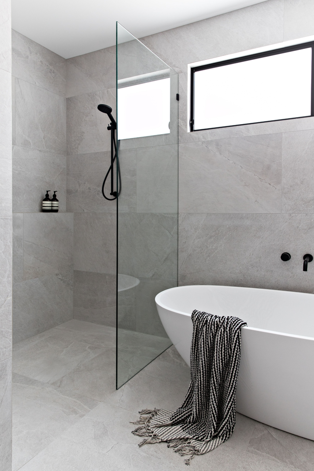 A contemporary bathroom showcasing a freestanding bathtub, sleek fixtures, and gray tiles.