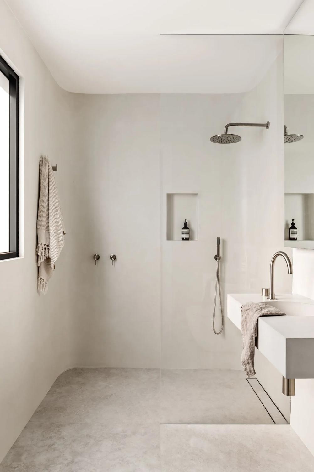 A minimalist bathroom featuring beige and white tones, large tiles, and natural light.