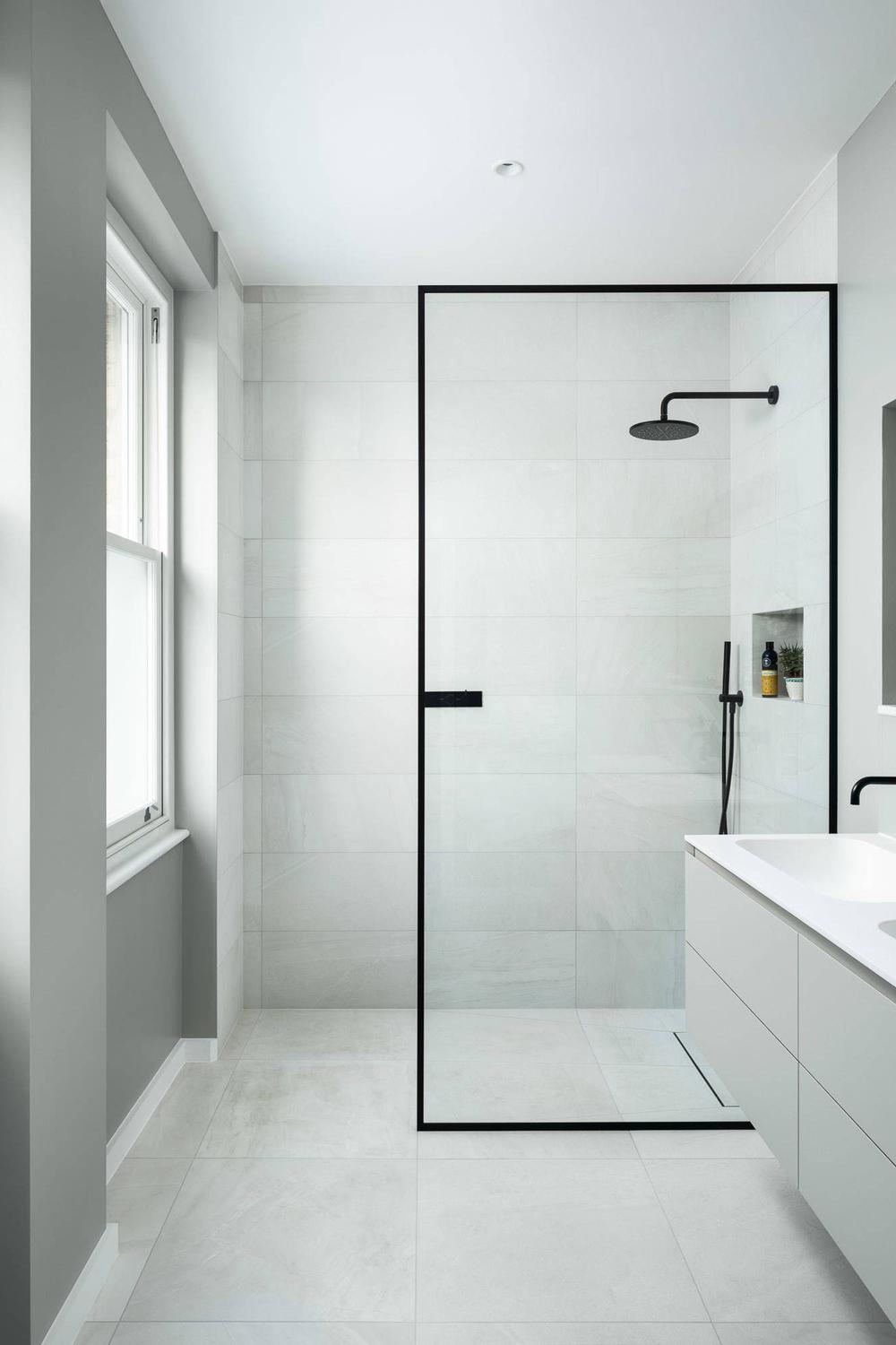 A modern bathroom with a frameless glass shower, light gray tiles, and a sleek vanity.