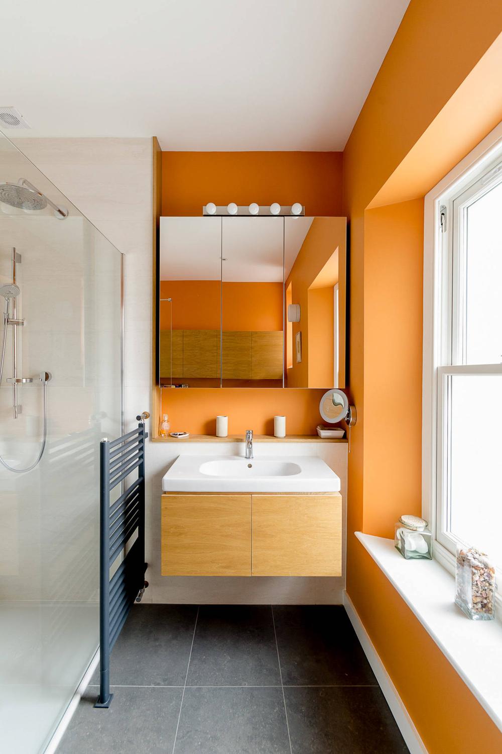 A modern bathroom with a vibrant orange wall and wooden vanity for a warm contrast.