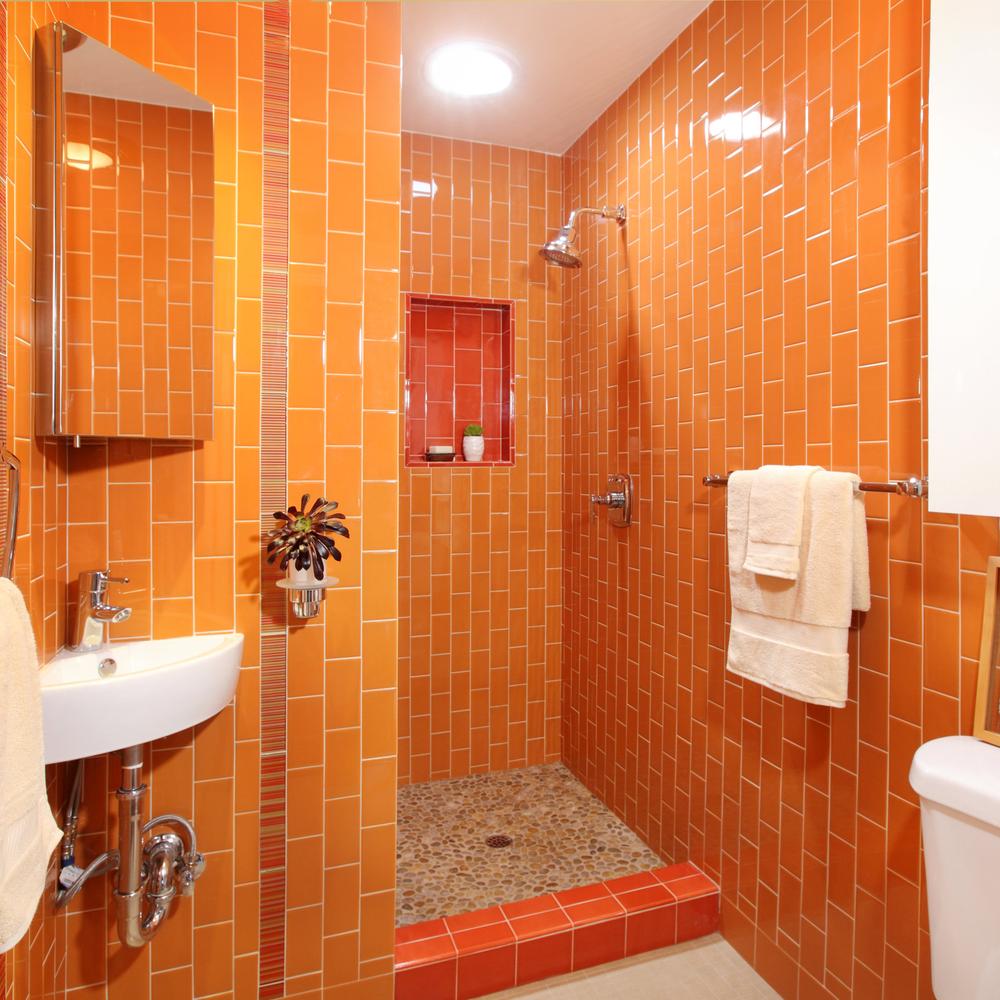A modern bathroom featuring glossy orange rectangular tiles and an open shower for a spa-like experience.