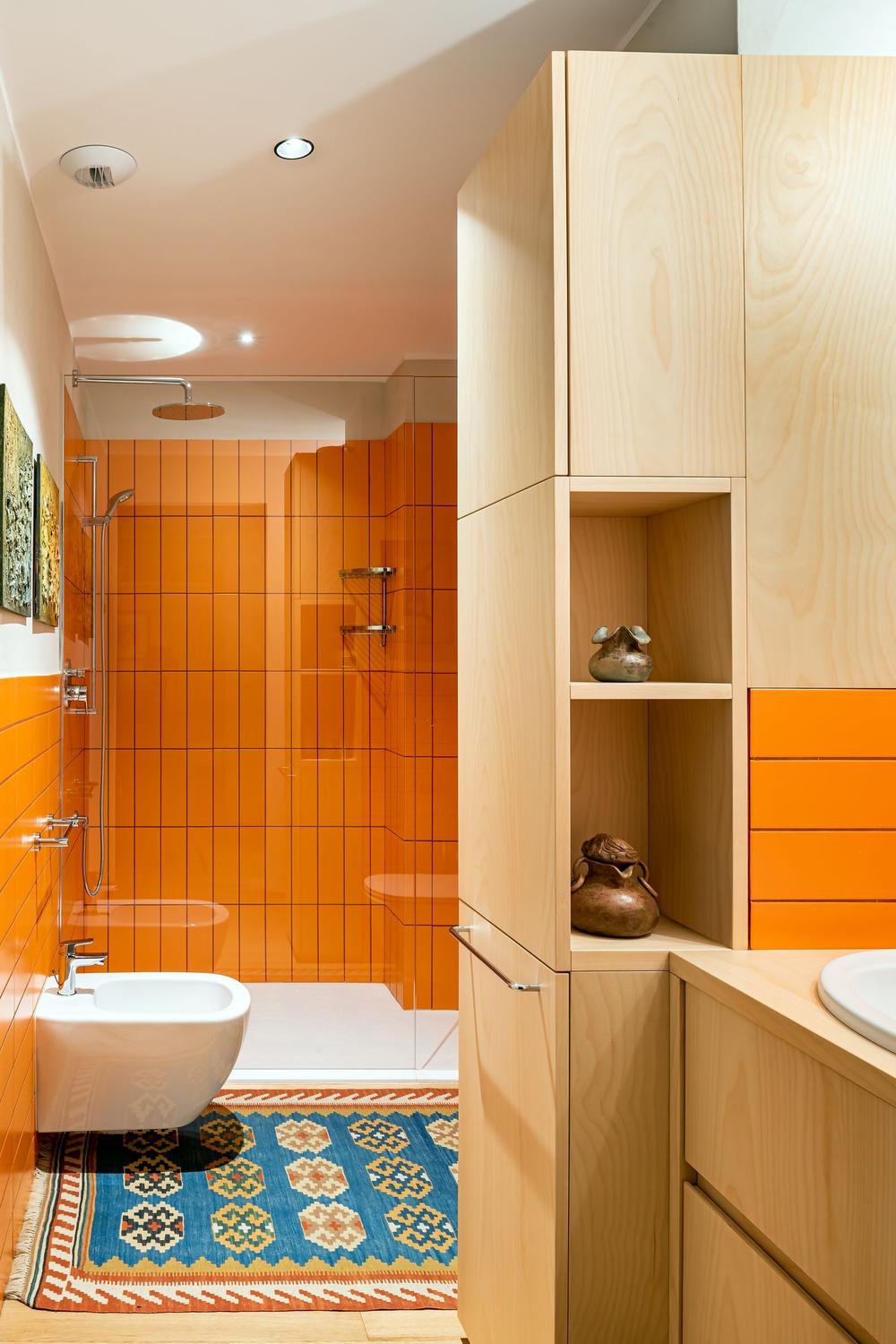 A modern bathroom featuring vibrant orange tiles and a spacious open shower.