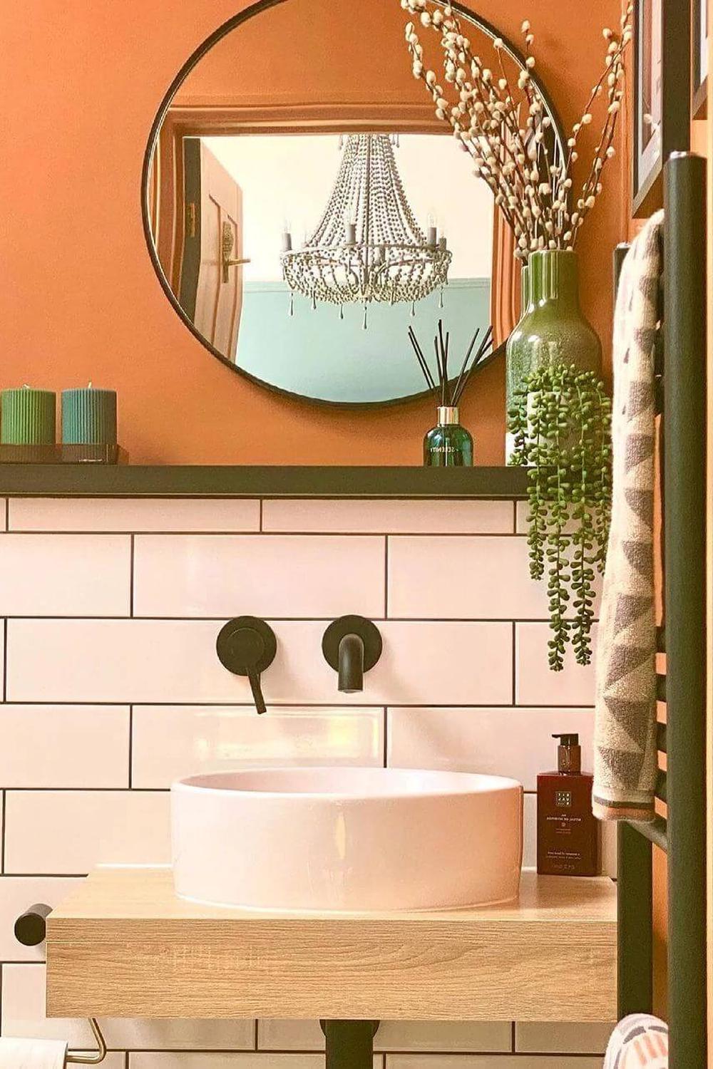 A contemporary bathroom featuring a vibrant orange wall and an elegant chandelier.