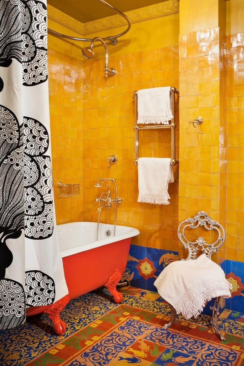 A vibrant and eclectic boho-style bathroom showcasing bright yellow walls, an orange bathtub, and patterned tiles.