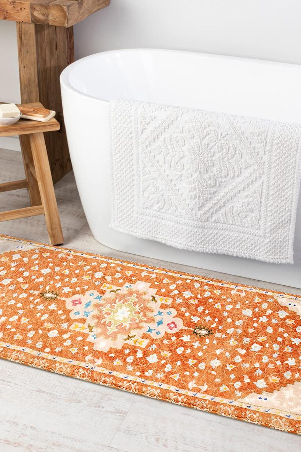 A modern yet cozy boho bathroom featuring an orange area rug and sleek freestanding bathtub.