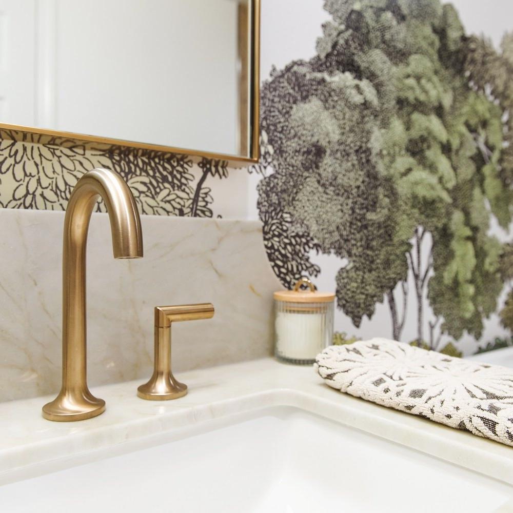 Baño con grifería de bronce y decoración botánica