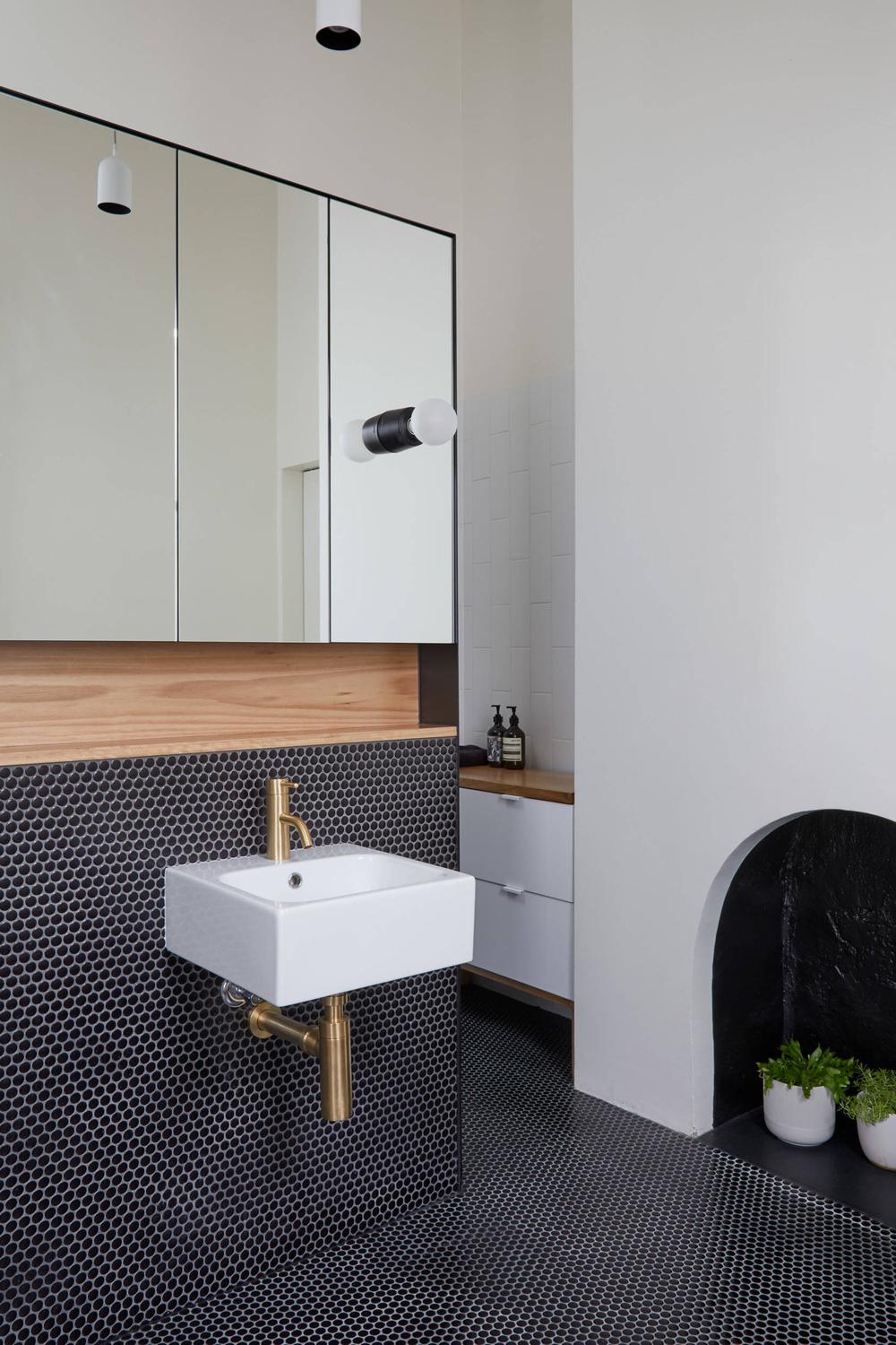 A chic bathroom showcasing black penny tile with modern fixtures and a stylish cabinet.