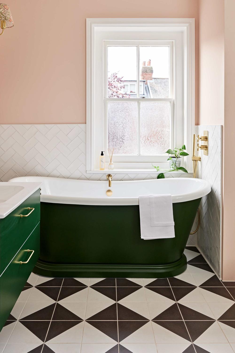 Stylish bathroom with dark green freestanding bathtub and pink accents