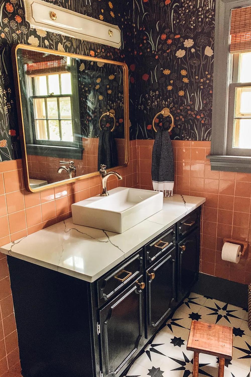Retro-inspired bathroom with dark floral wallpaper and black vanity contrasted against peach-colored tiles.