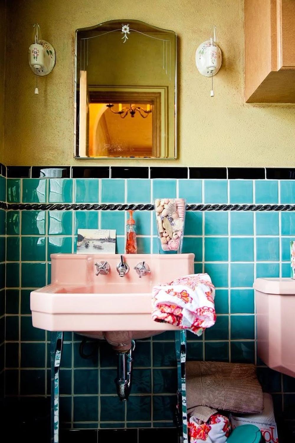 Retro bathroom blending vibrant teal tiles with vintage pink sink.