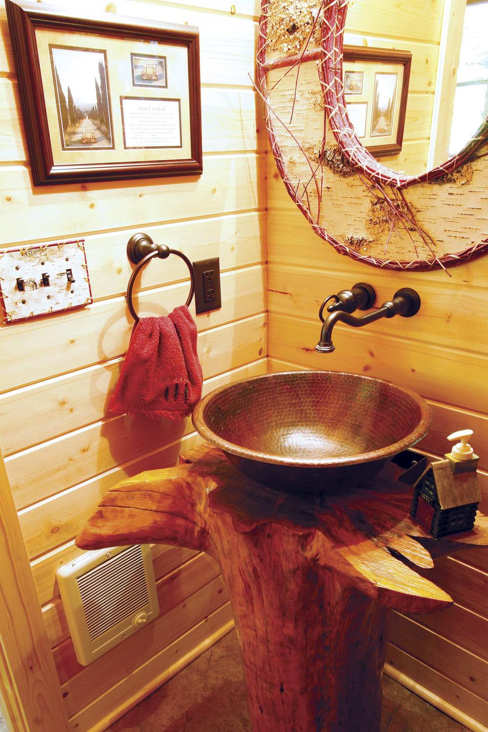 Rustic bathroom featuring an organic sink made from hammered copper bowl on wooden stump.