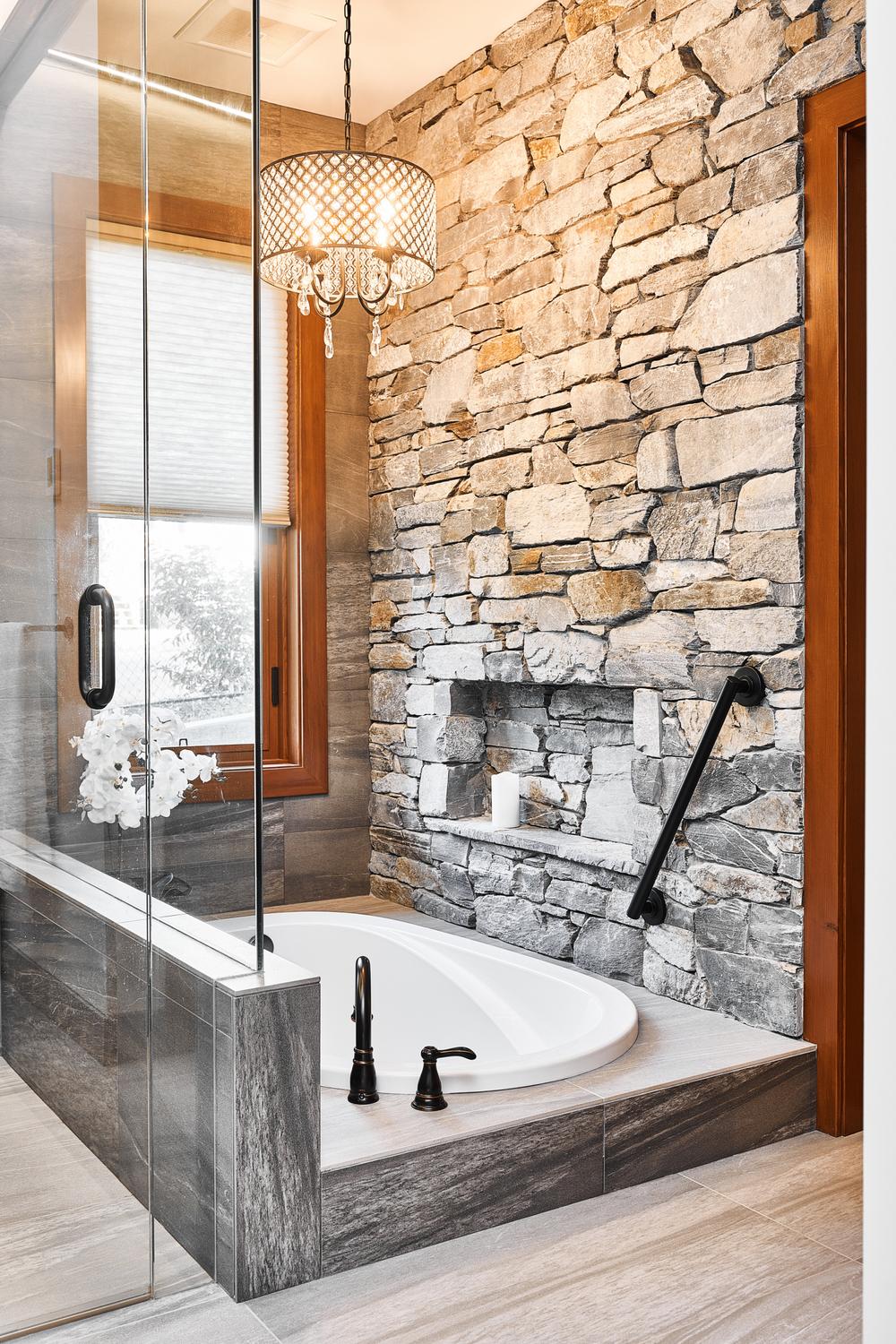 Natural stone walls, freestanding tub, and warm wood accents create a harmonious rustic bathroom.