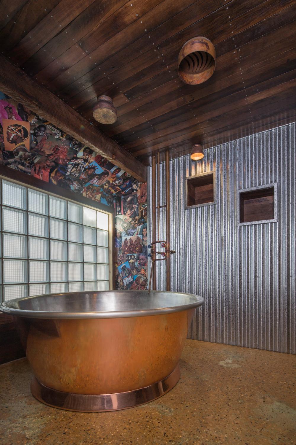 Striking rustic industrial bathroom showcasing a copper bathtub and artistic decor.