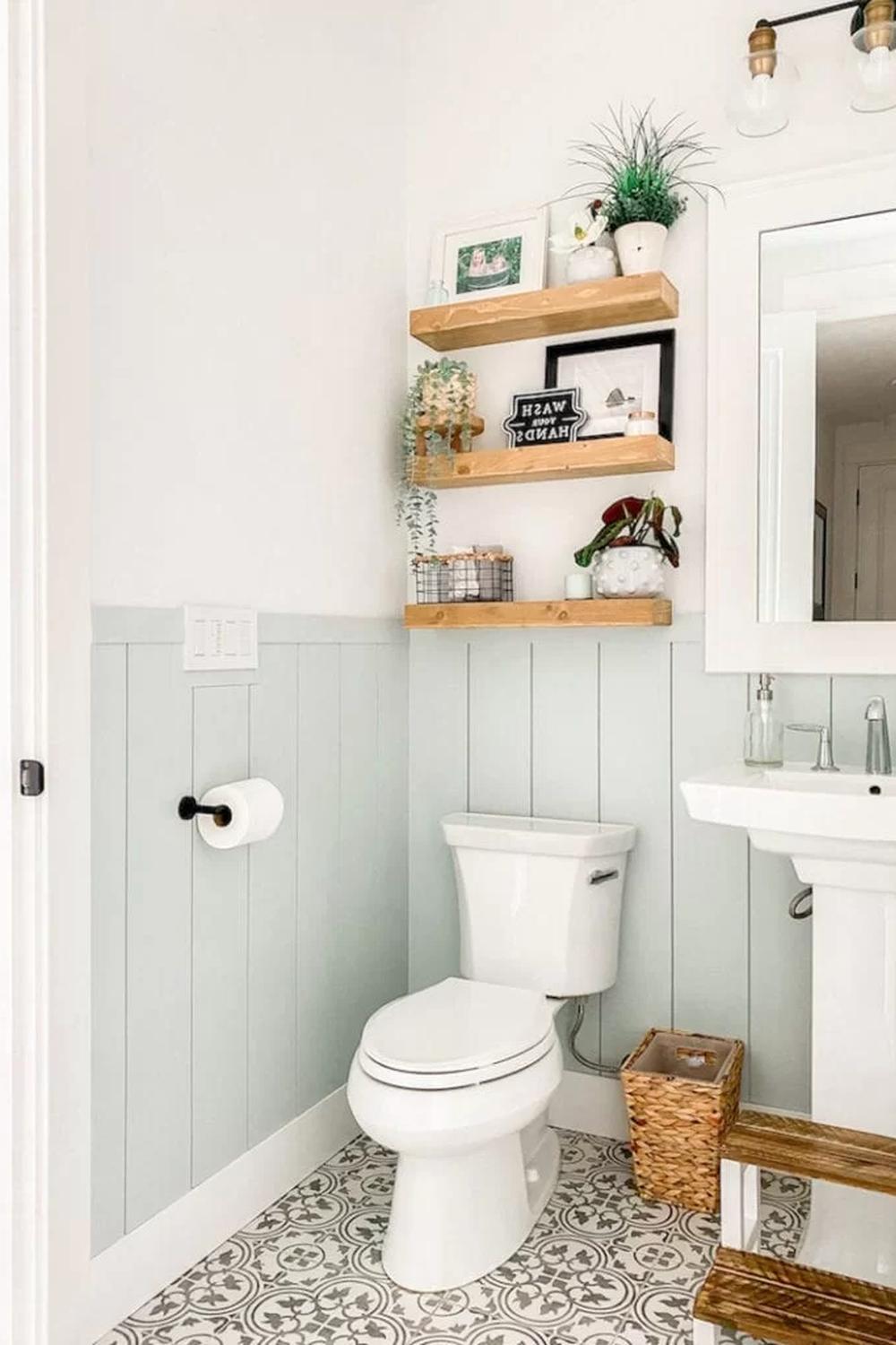 Modern bathroom with mint green shiplap paneling and wooden wall shelves decorated with plants and decorative signs.