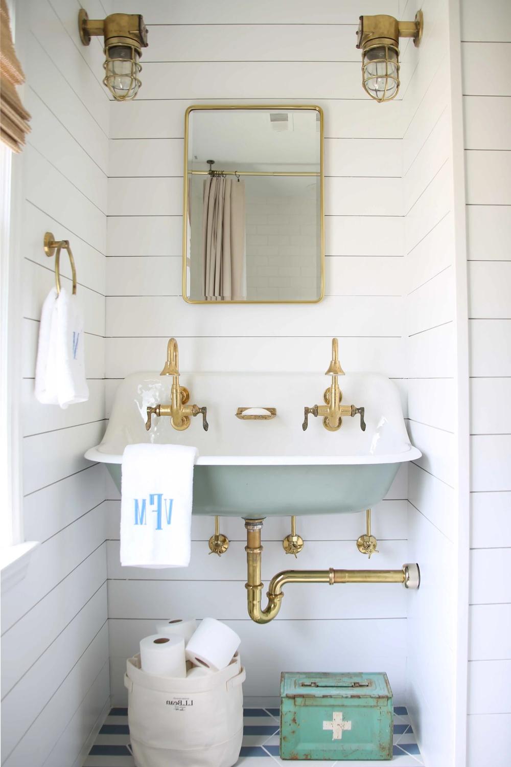 Elegant bathroom featuring white shiplap walls, a vintage wall-mounted sink, and industrial-style brass accents.