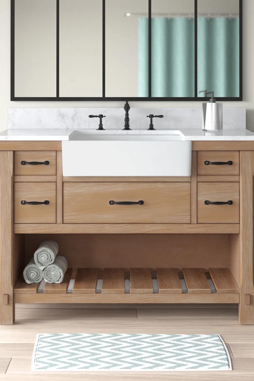 A farmhouse-style single bathroom vanity made from light wood, featuring a white marble top.